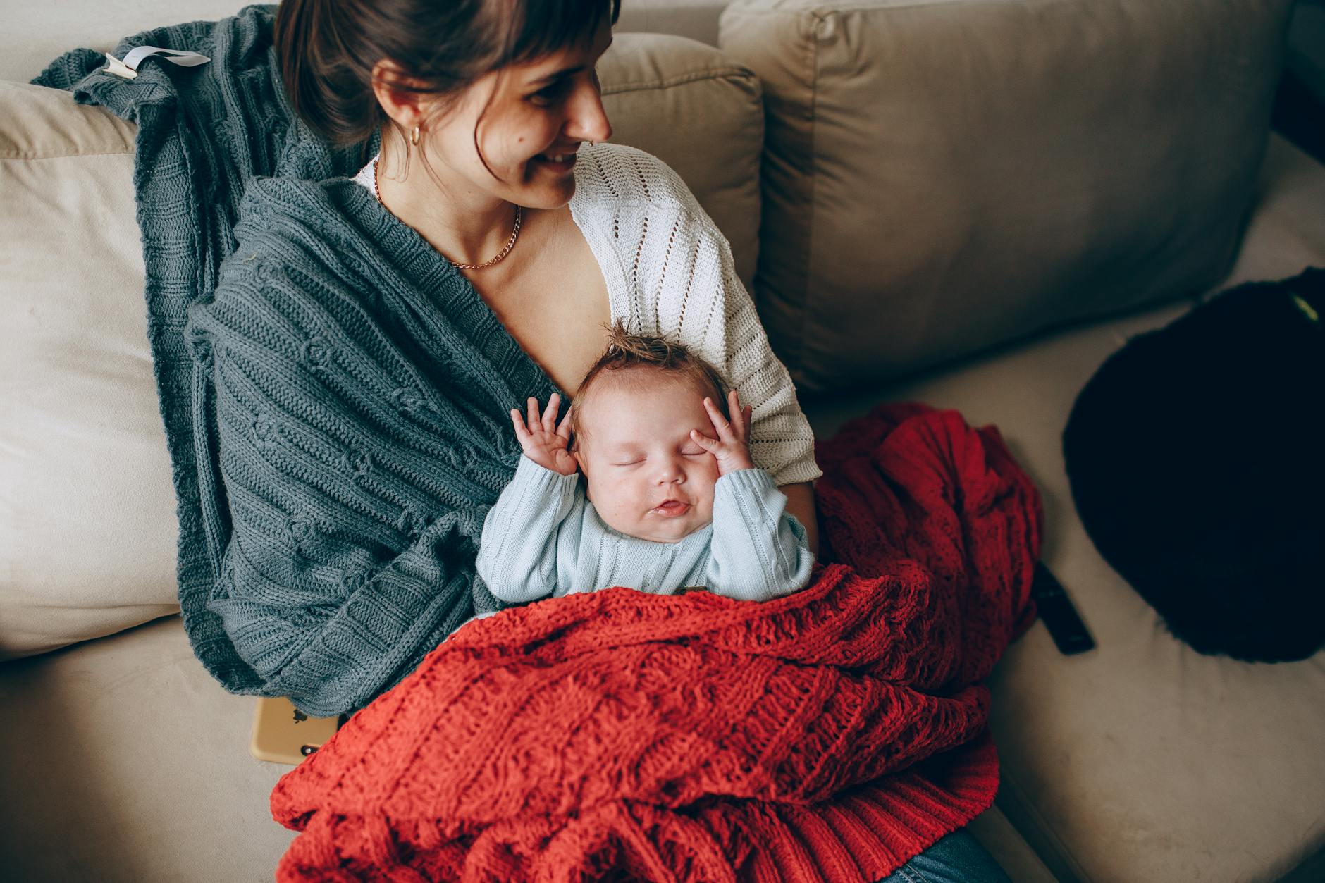 Mama przytulająca śpiące niemowlę owinięte kocem w domu